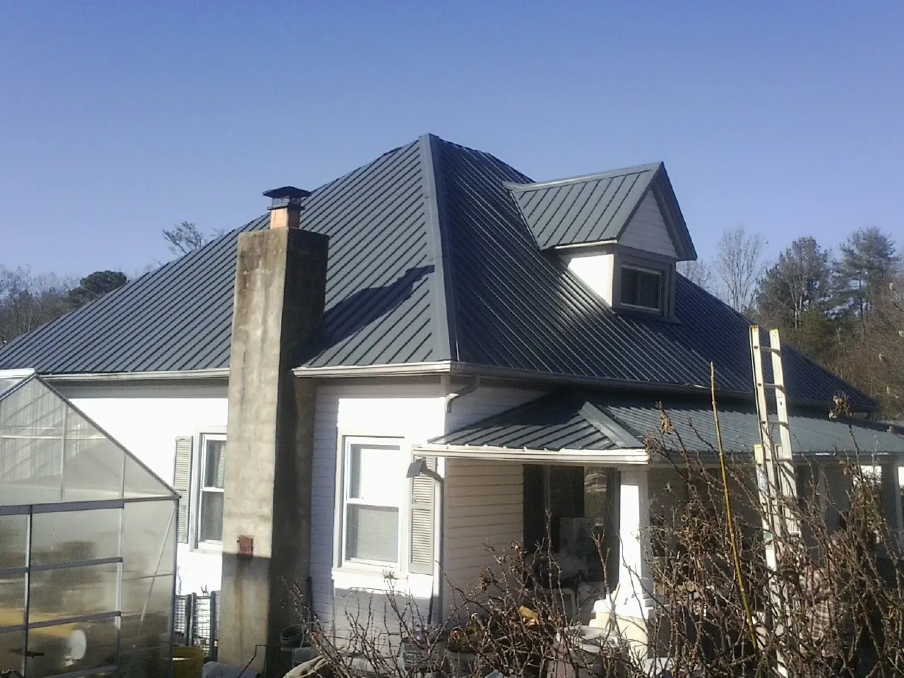 Dark blue standing seam metal roof on a white farmhouse with dormer — Slate & Tile Roof Repair by Roofing Brothers in Moretown