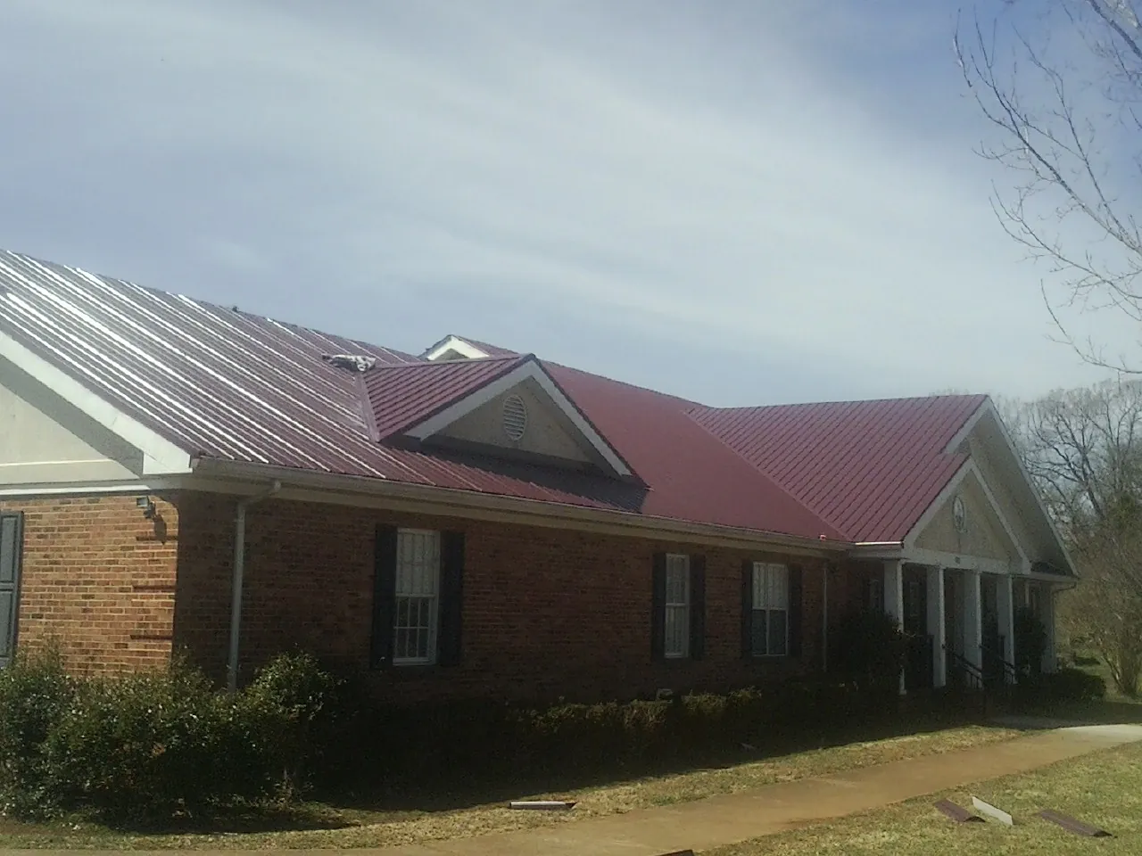 Red metal roof with gabled entries on a long brick building, from a Hail Damage Roof Repair job in Moretown