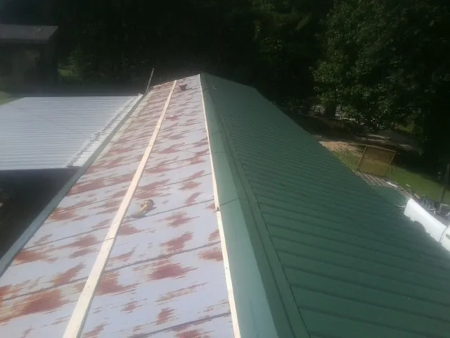 Old rusted panels beside newly installed green metal roofing — Wind Damage Roof Repair by Roofing Brothers in Moretown