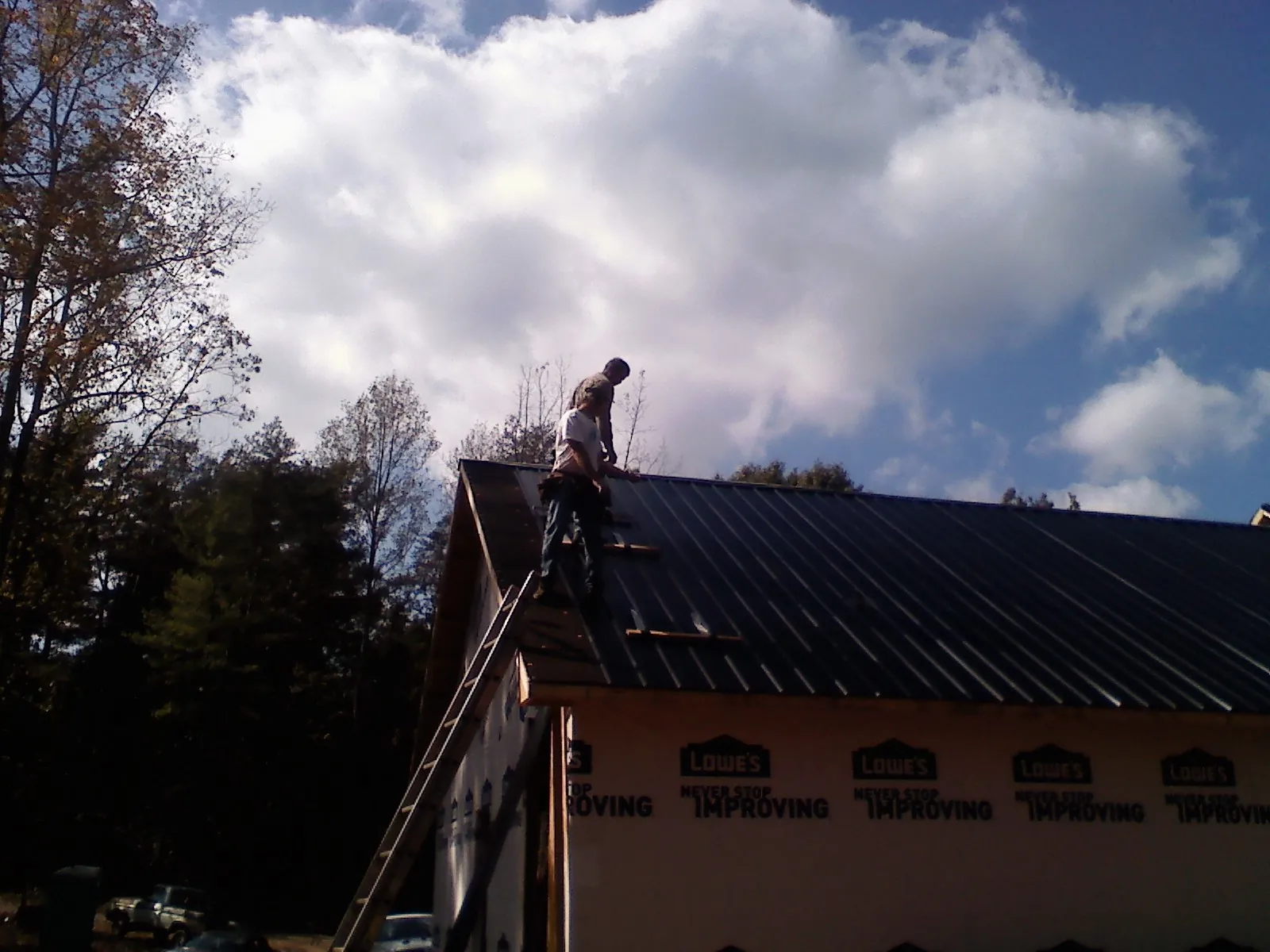 Roofer fastening dark metal panels high against a cloudy sky, from a Roof Inspection job in Moretown