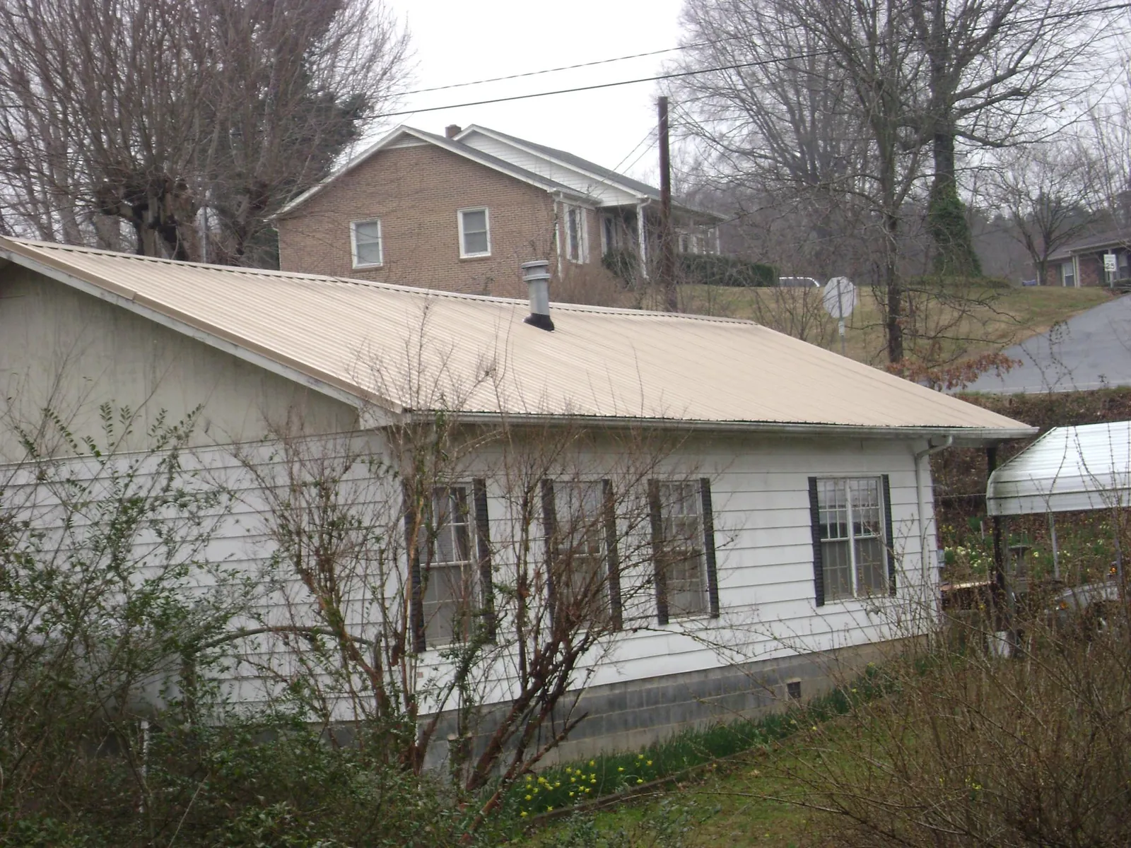 Tan metal roof on a white sided house set into a hillside — Commercial Roofing by Roofing Brothers in Moretown
