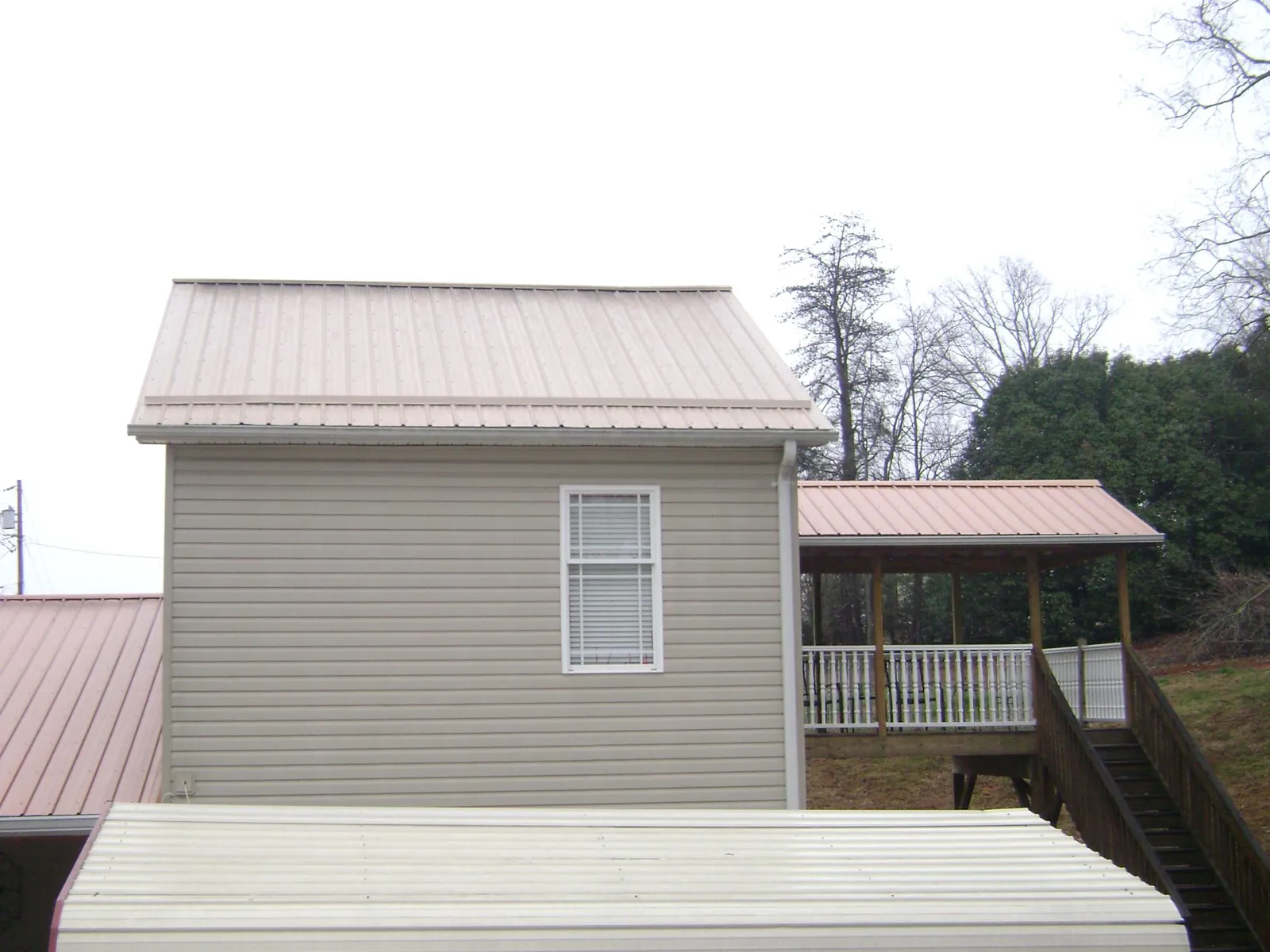 Tan metal roofs on a two story addition and attached porch, from a Roof Replacement job in Moretown